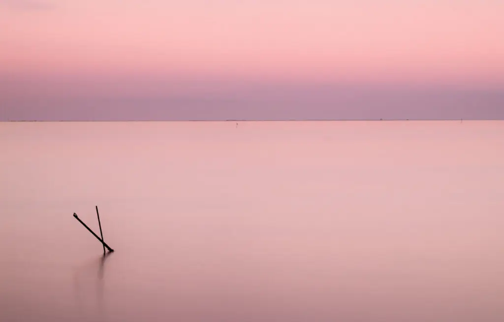 Fotografia pictòrica del silenci, mar i cel fusionant-se en un horitzó rosat intens amb estructures metàliques en forma de creu al mar