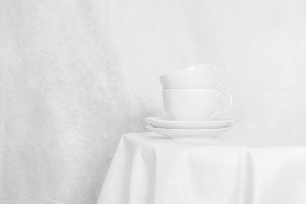 Fotografia artística minimalista en blanc: dues tasses sobre taula blanca amb paret blanca de fons. Minimalisme domèstic.