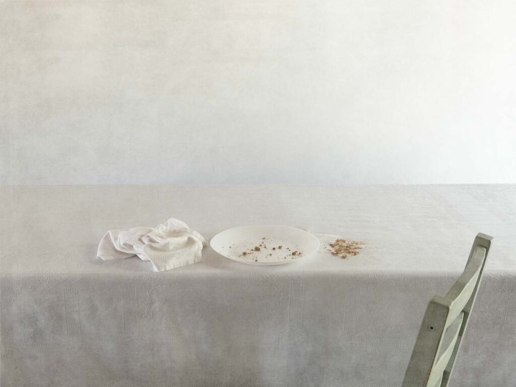 Fotografia de natura morta minimalista amb una taula, un plat amb molles, un tovalló i el respatller d'una cadira