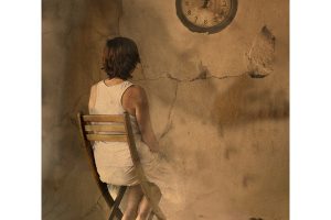 Figura femenina en penombra amb llum suau, fotografia artística sobre el temps i l’espera.