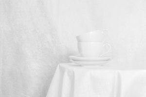 Fotografia artística minimalista en blanc: dues tasses sobre taula blanca amb paret blanca de fons. Minimalisme domèstic.